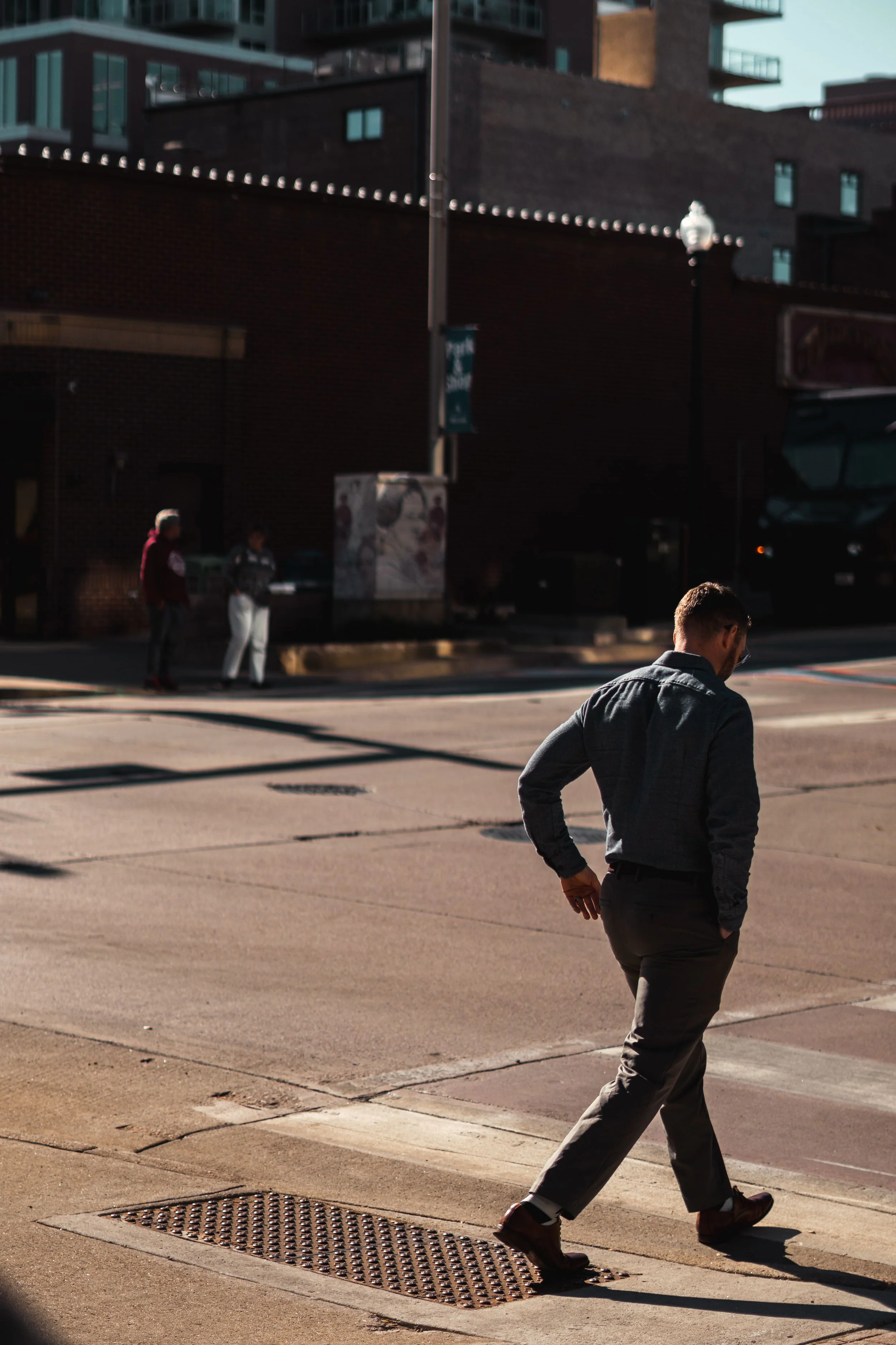 A person in black walking through a sunlit urban plaza.