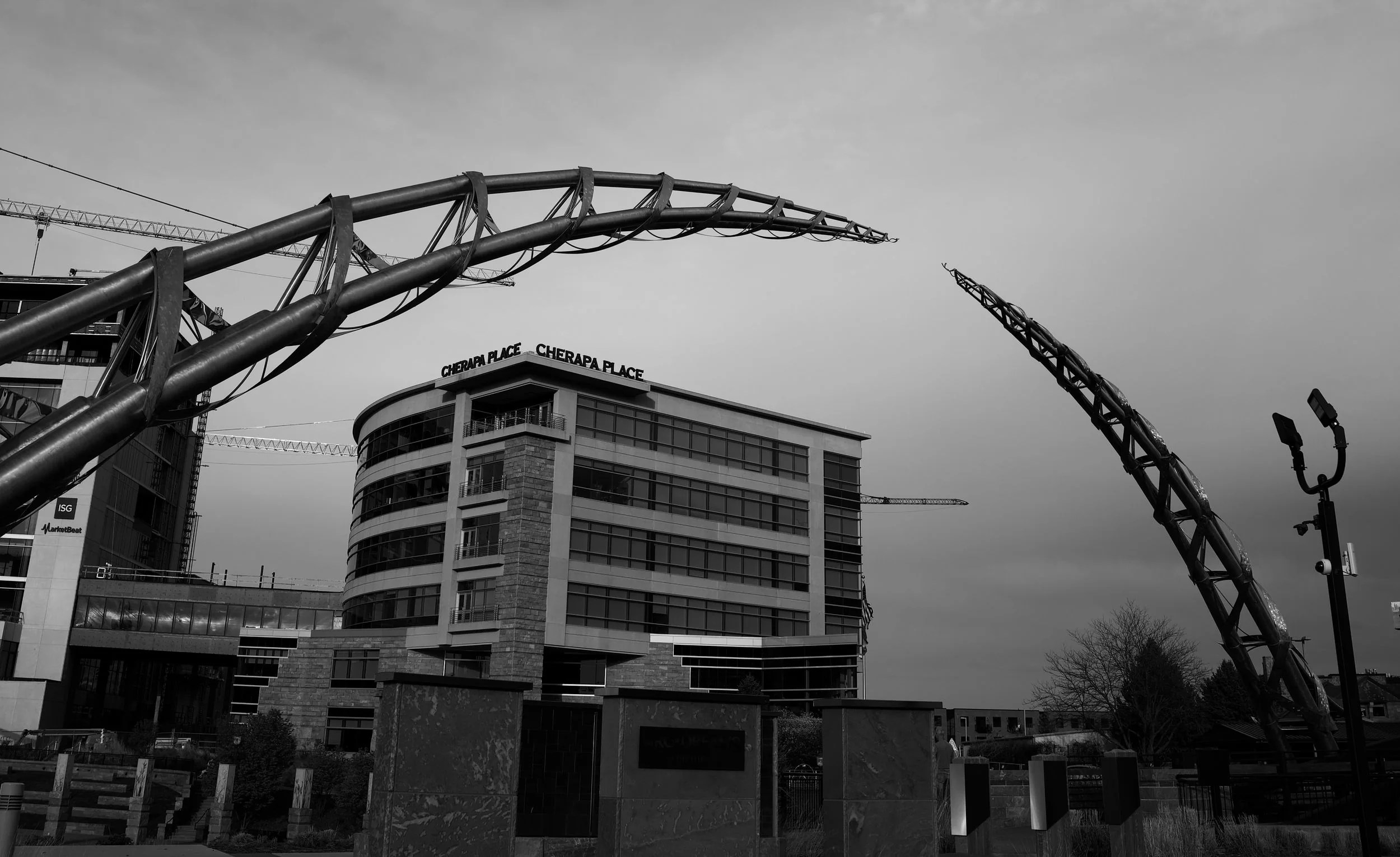Black-and-white cityscape with sweeping metal sculptures framing a modern building.