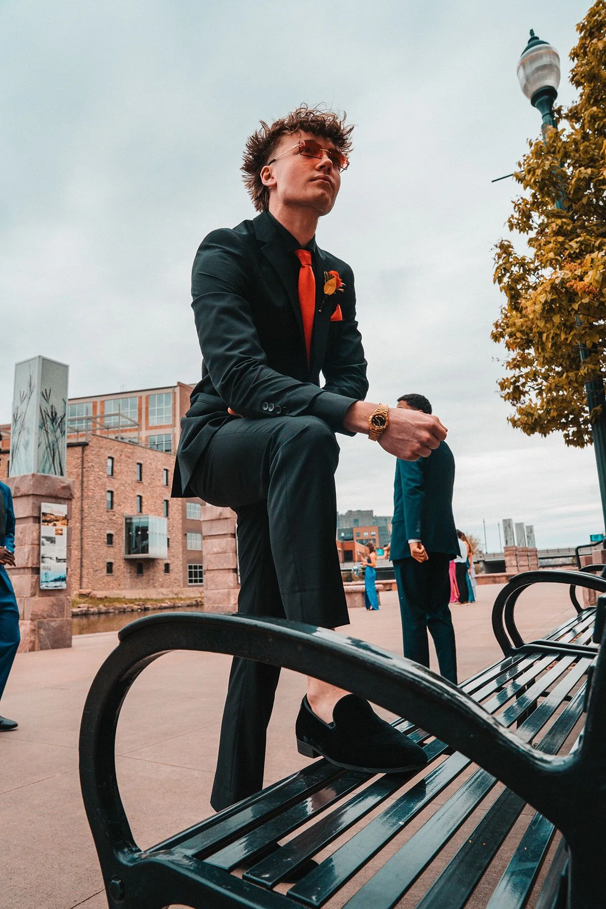 A young man in a black suit standing beside an urban railing.