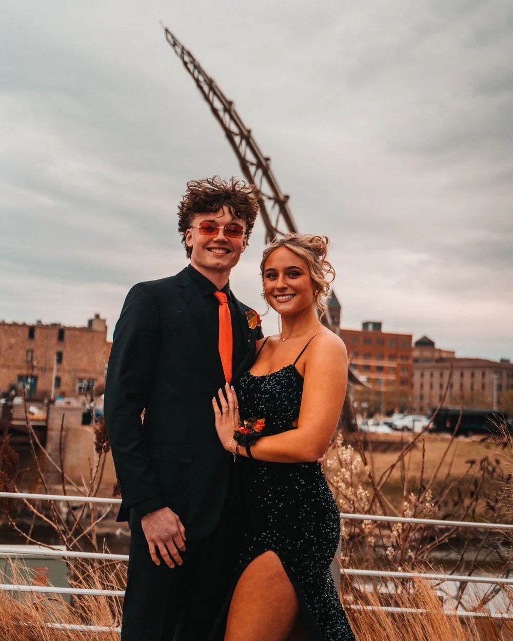 A formally dressed couple posing together on a rooftop at sunset.