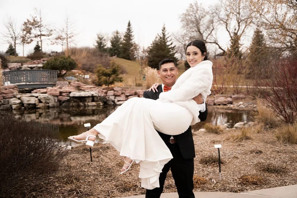 A groom carrying his bride beside a landscaped pond.