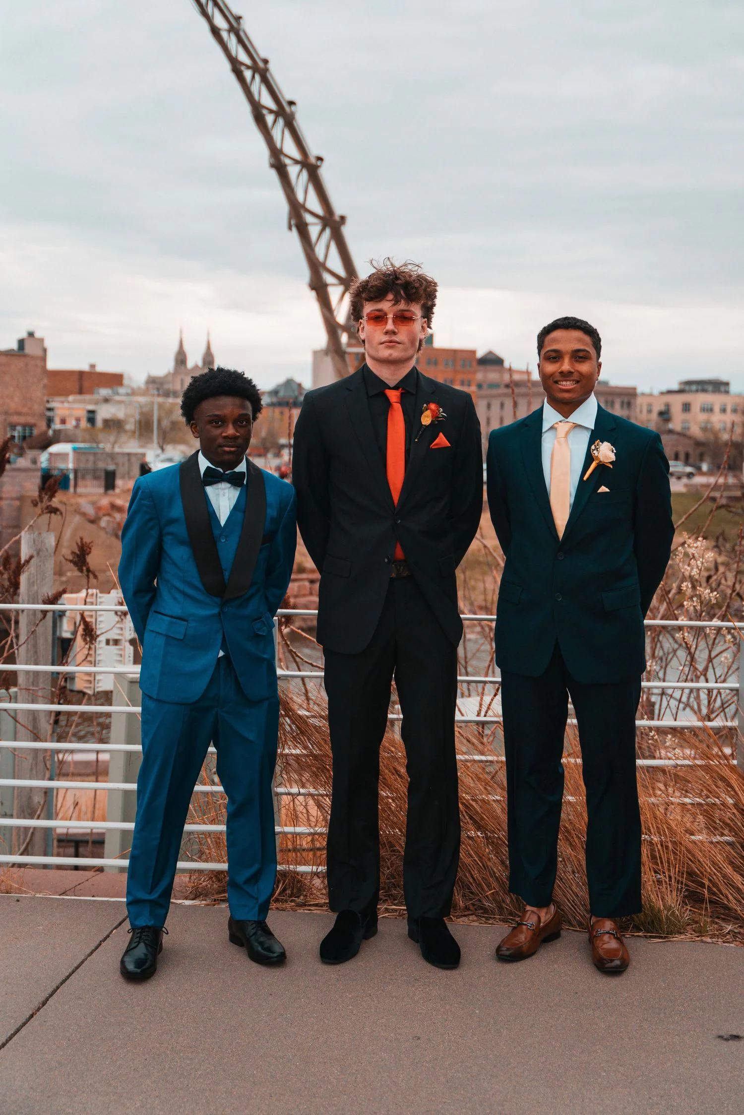 Three young men in suits posing together on a rooftop.